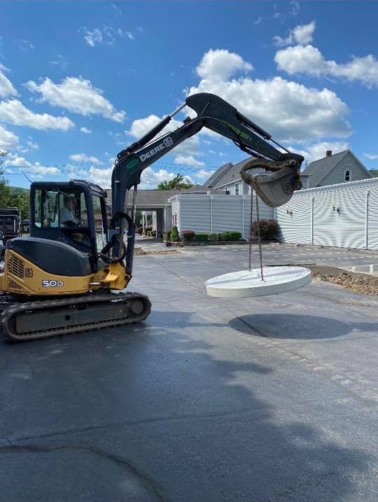 A yellow and black excavator is lifting a concrete circle in a parking lot.