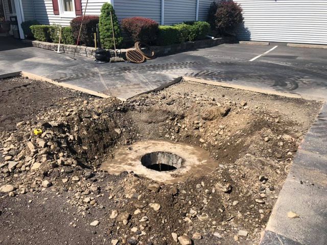A hole in the ground in a parking lot next to a house.