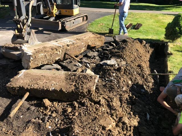 A man with a shovel is digging in the dirt in front of an excavator