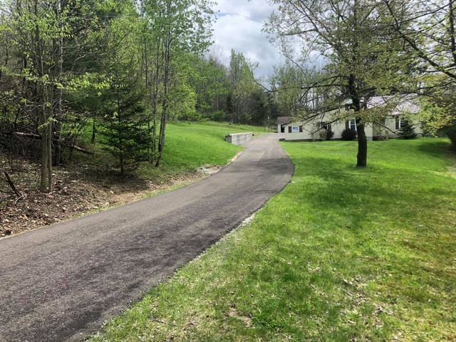 A driveway leading to a house surrounded by trees and grass.