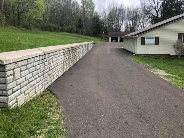 A brick wall along the side of a road leading to a house.