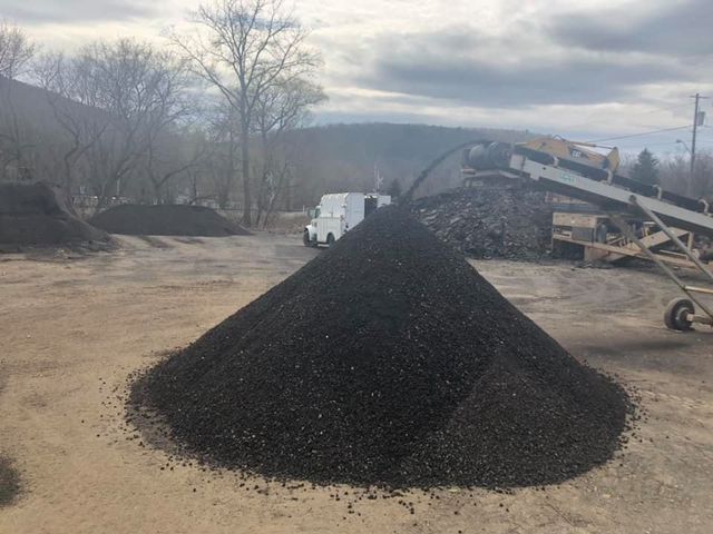 A pile of black gravel is sitting on top of a dirt field.