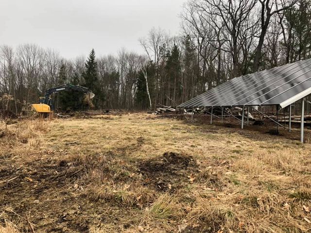 A row of solar panels are sitting in a field with trees in the background.