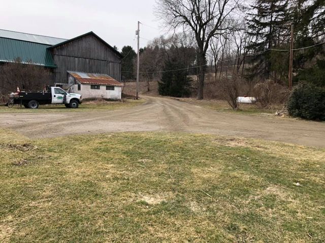 A white truck is parked on the side of a dirt road next to a barn.
