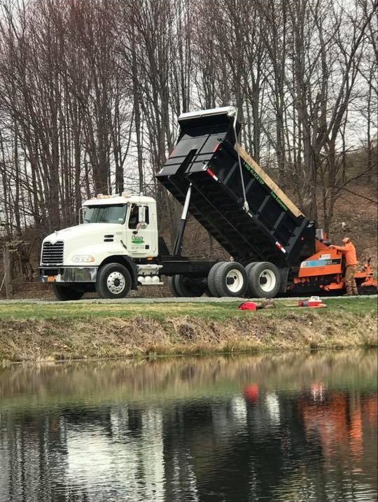 A dump truck is parked on the side of the road next to a body of water.