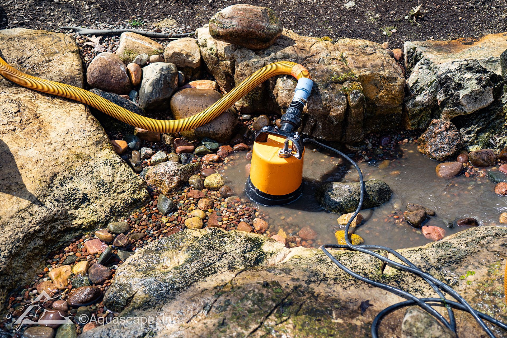 A hose is attached to a pump in a rocky area.