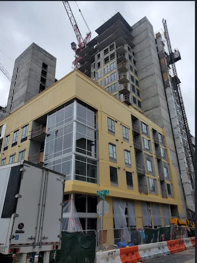 Construction site with partially built yellow building and tall tower; cranes and trucks.