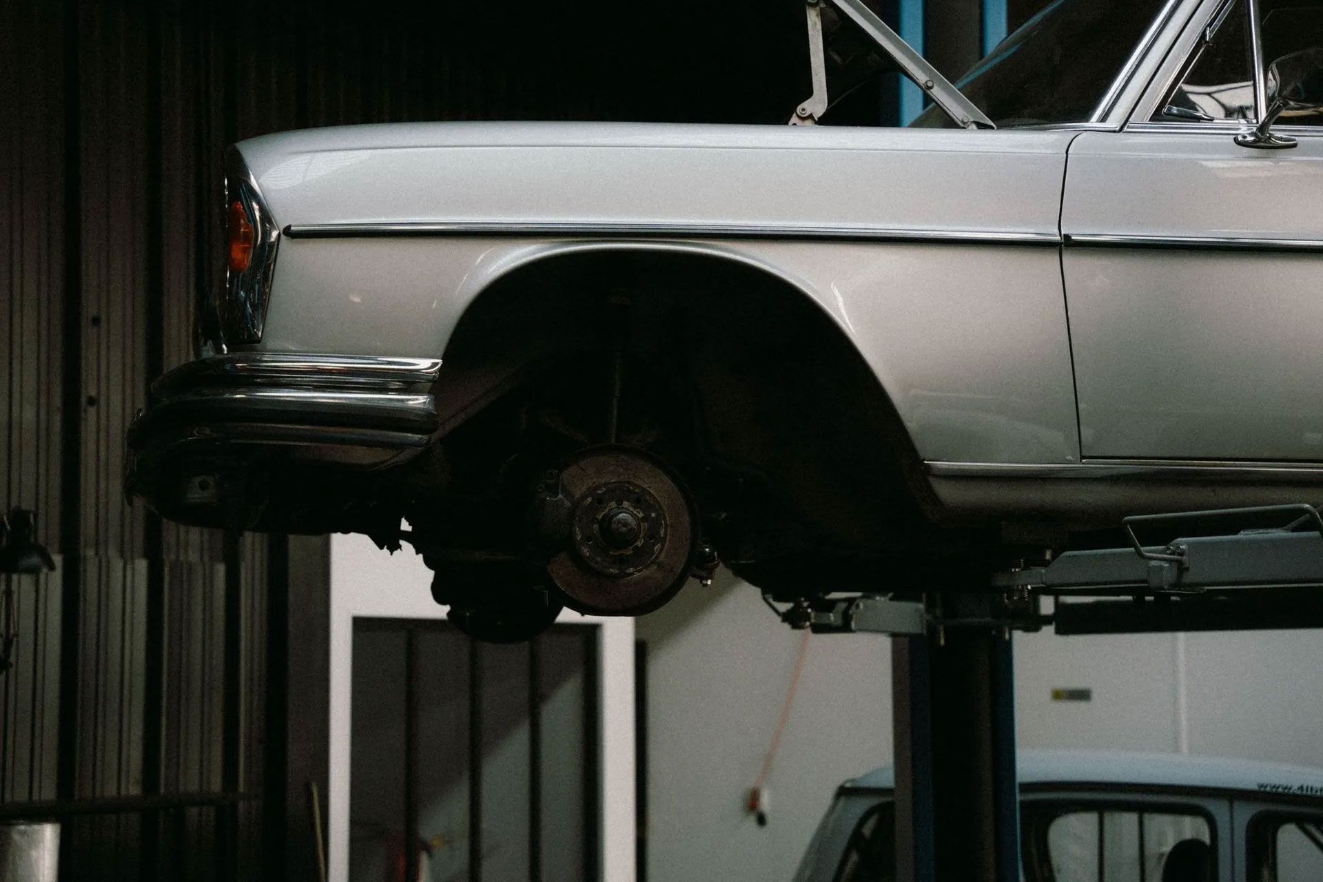 Car lifted on a hoist in an auto repair garage, front wheel removed.
