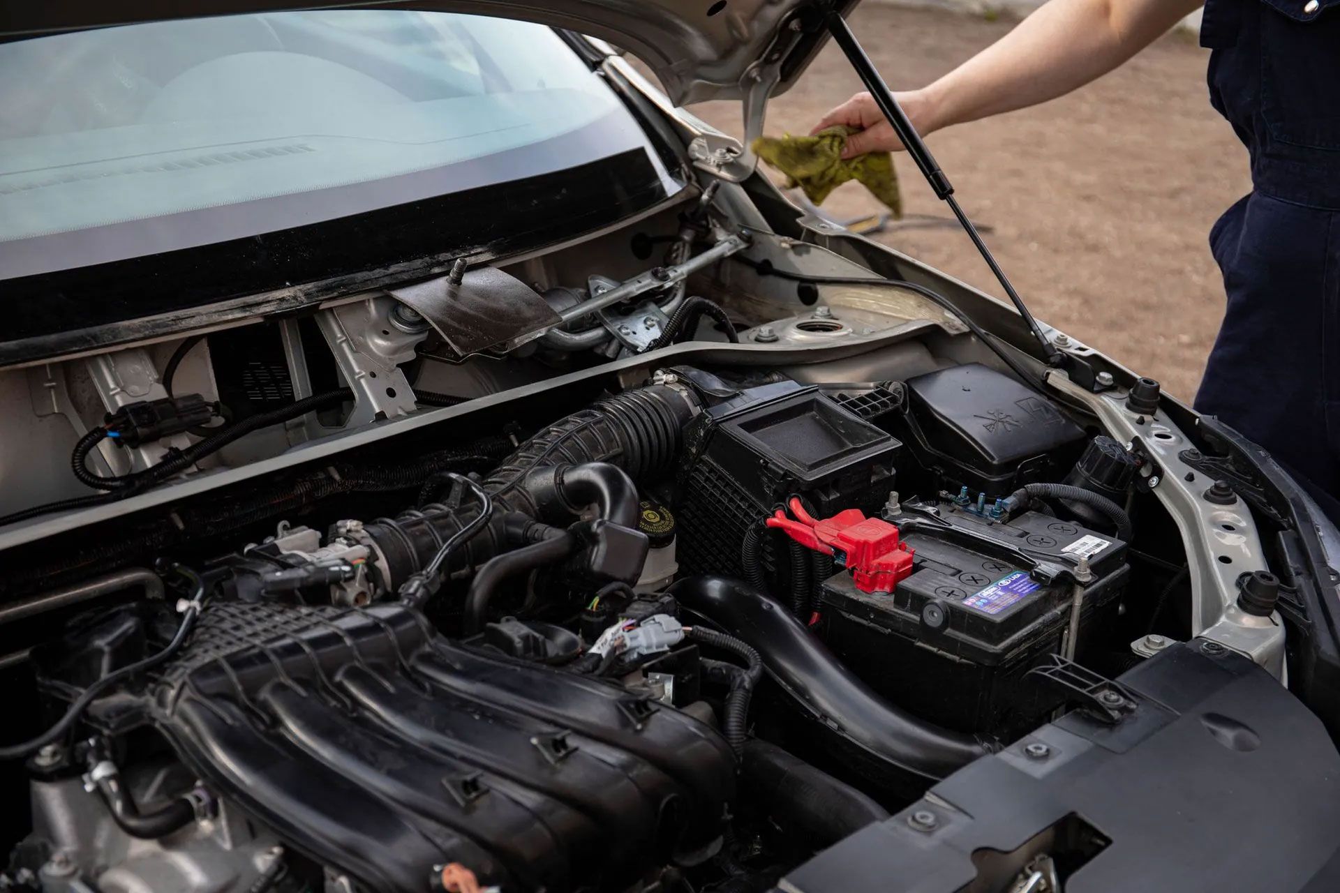 Open car hood with engine bay exposed and a person inspecting the battery area