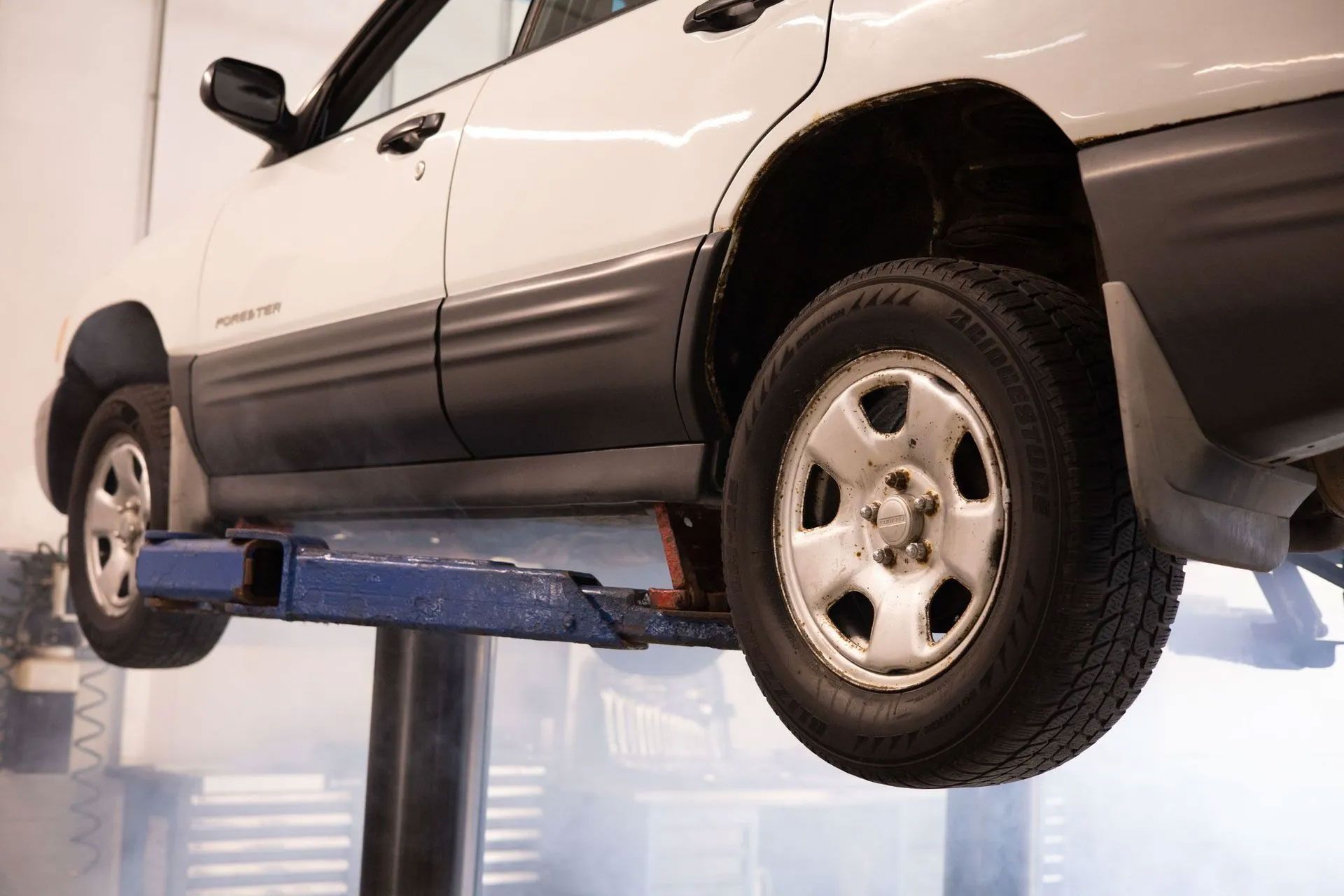 White SUV lifted on a blue hydraulic car lift in an auto repair shop