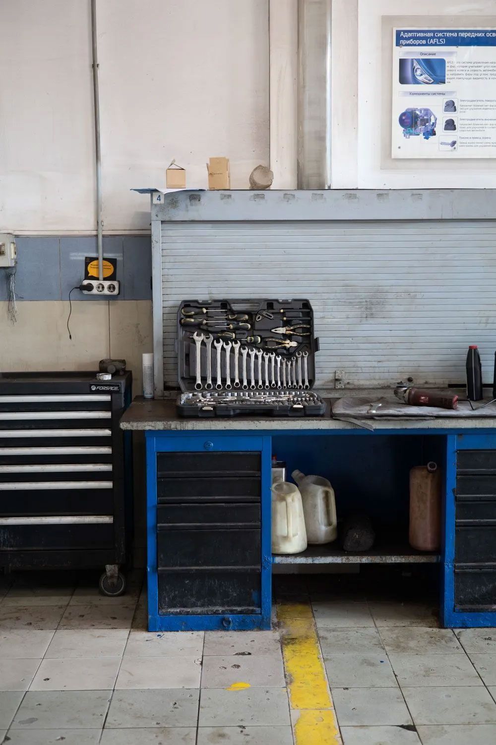 Industrial workshop bench with tools, blue storage cabinets, and a black tool chest on the left