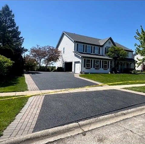 Suburban house with wide dark driveway, green lawn, and a mailbox under a sunny blue sky