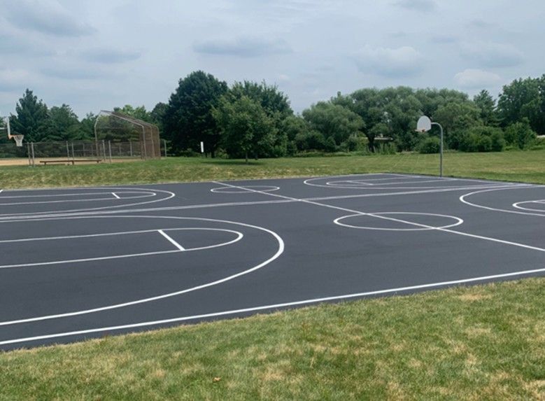 Empty outdoor basketball court with white lines on blacktop under a cloudy sky.