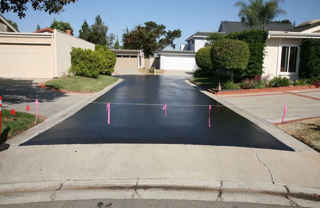 Fresh black asphalt driveway in a residential neighborhood, marked with pink flags for a paving project