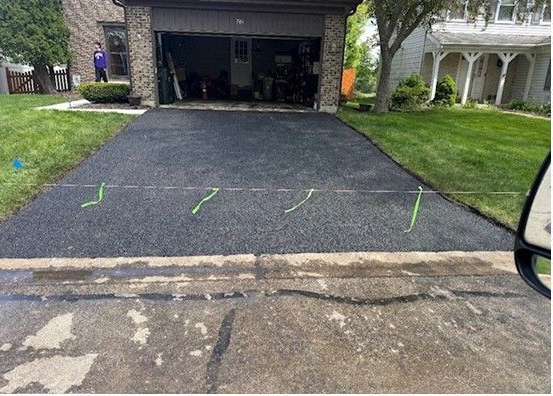 Freshly paved black asphalt driveway leading to an open garage beside a grassy yard.