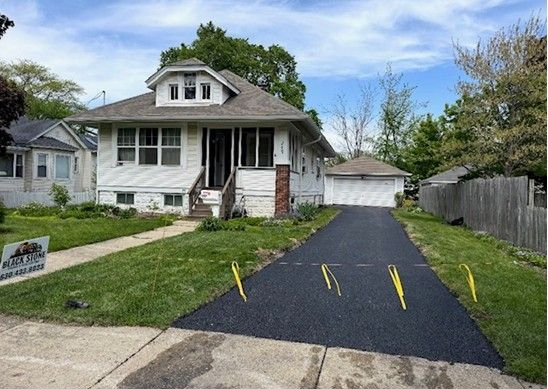 House with fresh black driveway patch and yellow markings in front of a white home on a residential street