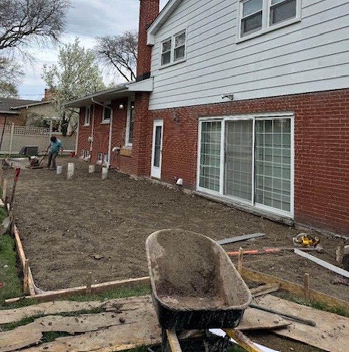 Backyard renovation with dirt yard, wheelbarrow, and worker near a brick-and-siding house