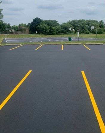 Empty parking lot with yellow lines and green trees under a cloudy sky