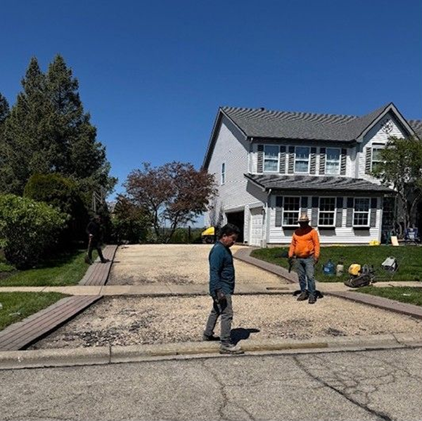Two workers standing in a driveway beside a white house under a clear blue sky