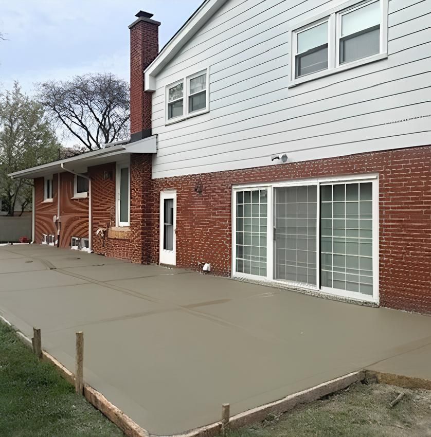 Brick and white house exterior with a large concrete patio and sliding glass doors