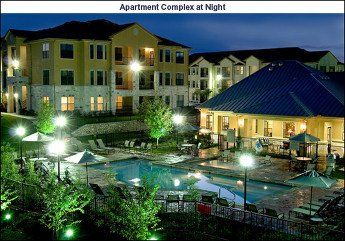Apartment complex at night. Pool, lounge chairs, building with lights, dark sky.