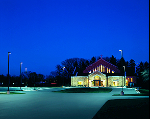 Church exterior at night, illuminated by streetlights, parking lot in the foreground.