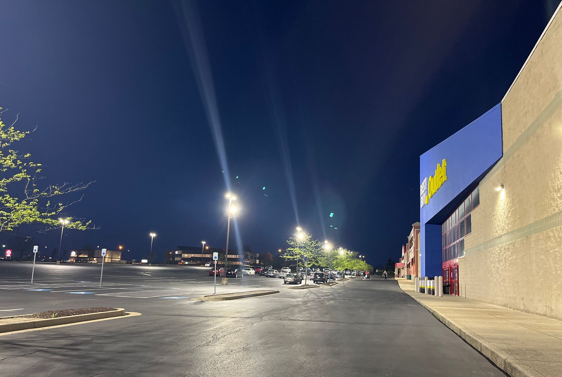 Nighttime view of a mostly empty parking lot next to a building with a blue sign. Streetlights illuminate the scene.