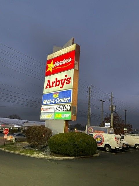 Signpost with Hardee's, Arby's, and other businesses at dusk.