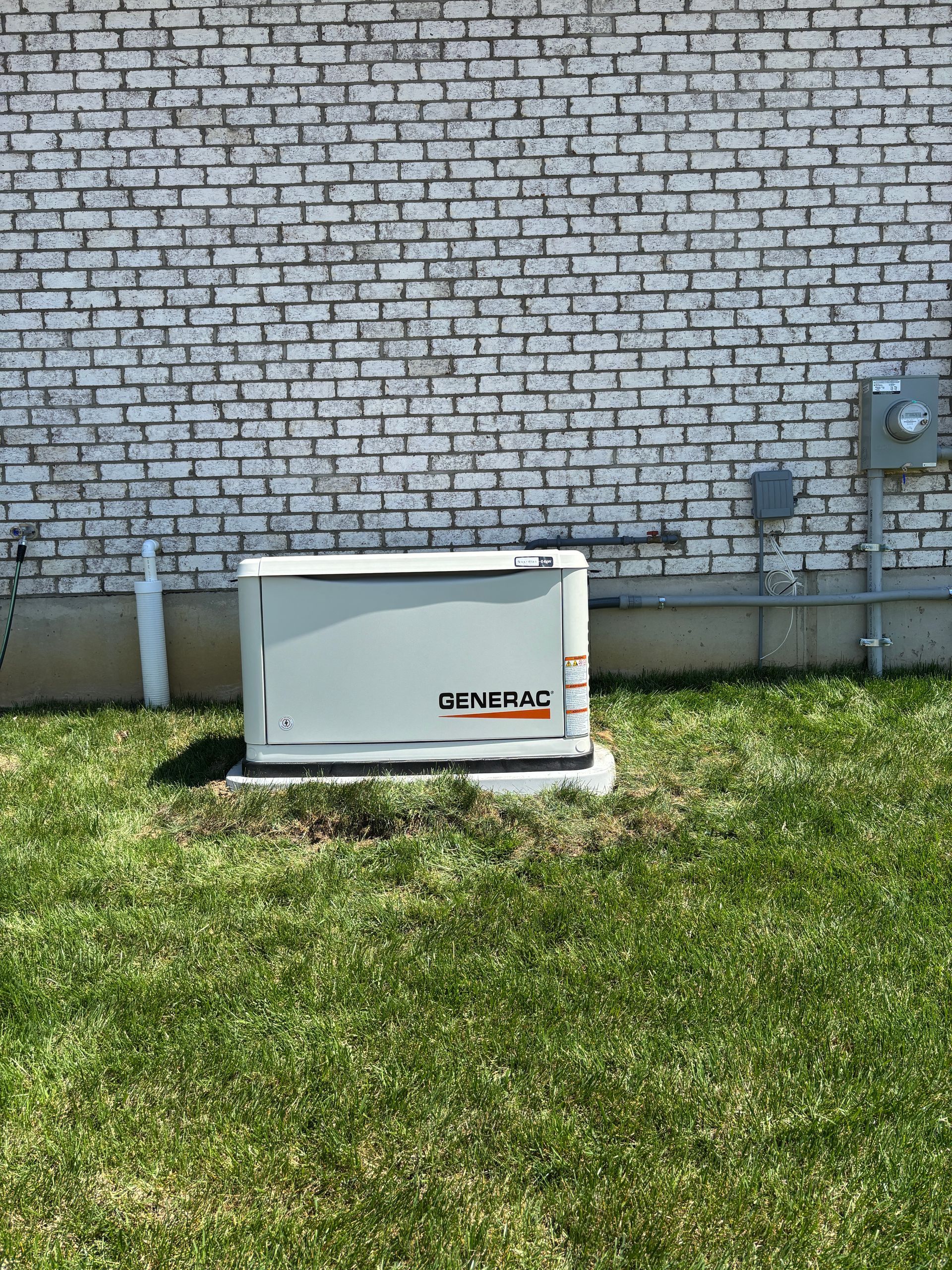 Generac generator near a white brick building. Green grass in front.