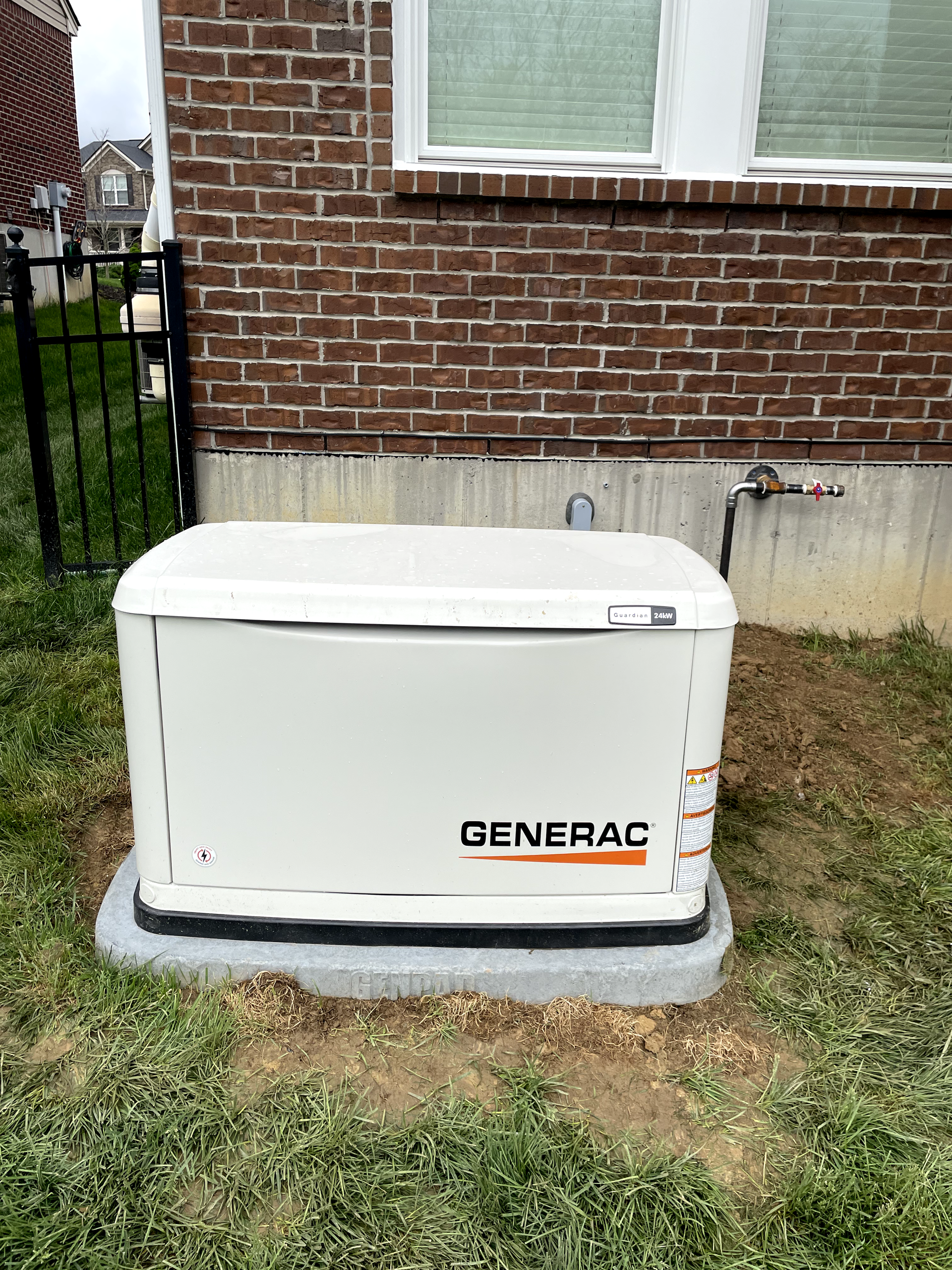 A Generac generator on a concrete pad next to a brick building and green grass.