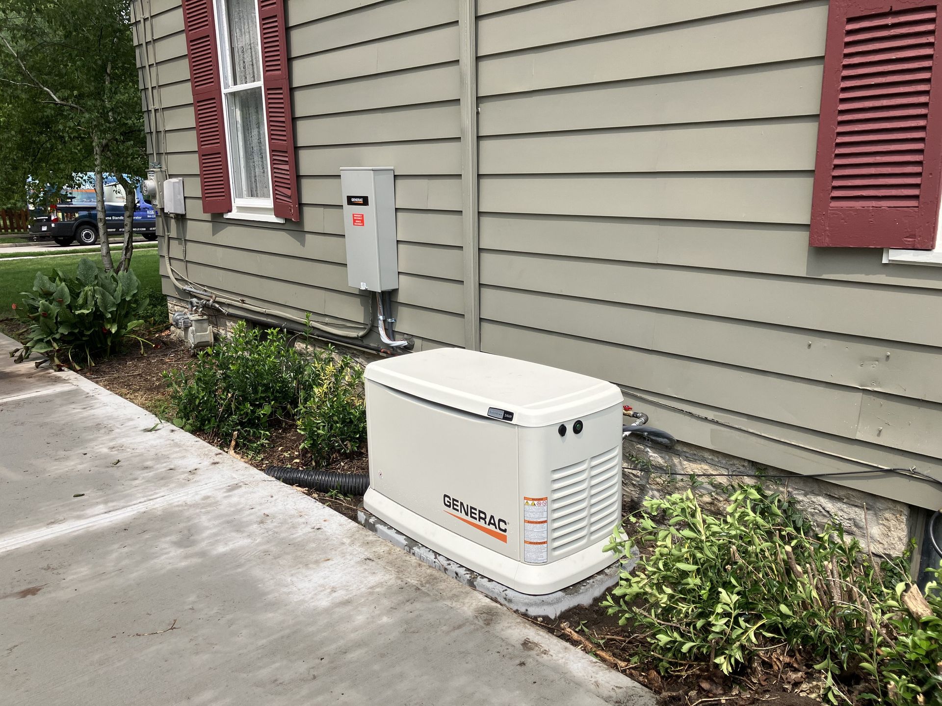 A standby generator installed outside a beige house, next to a gray electrical box.