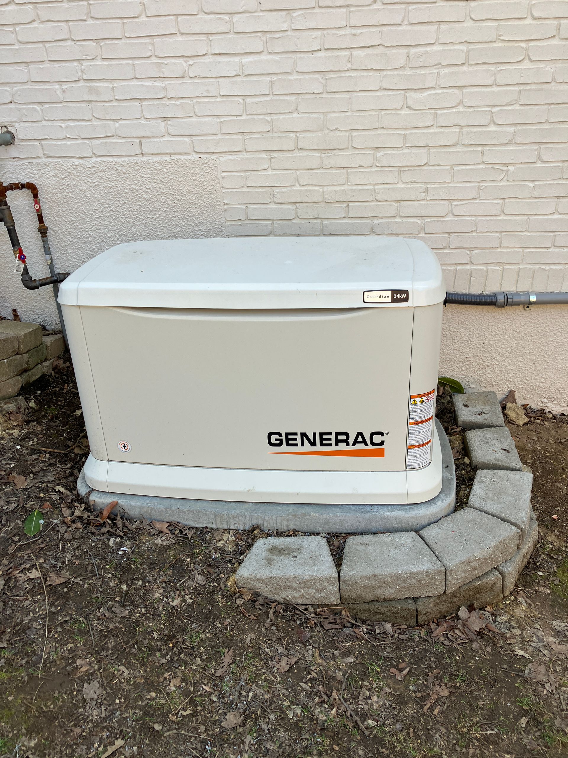 A beige Generac generator outside a building, set on a concrete pad with a surrounding brick border.