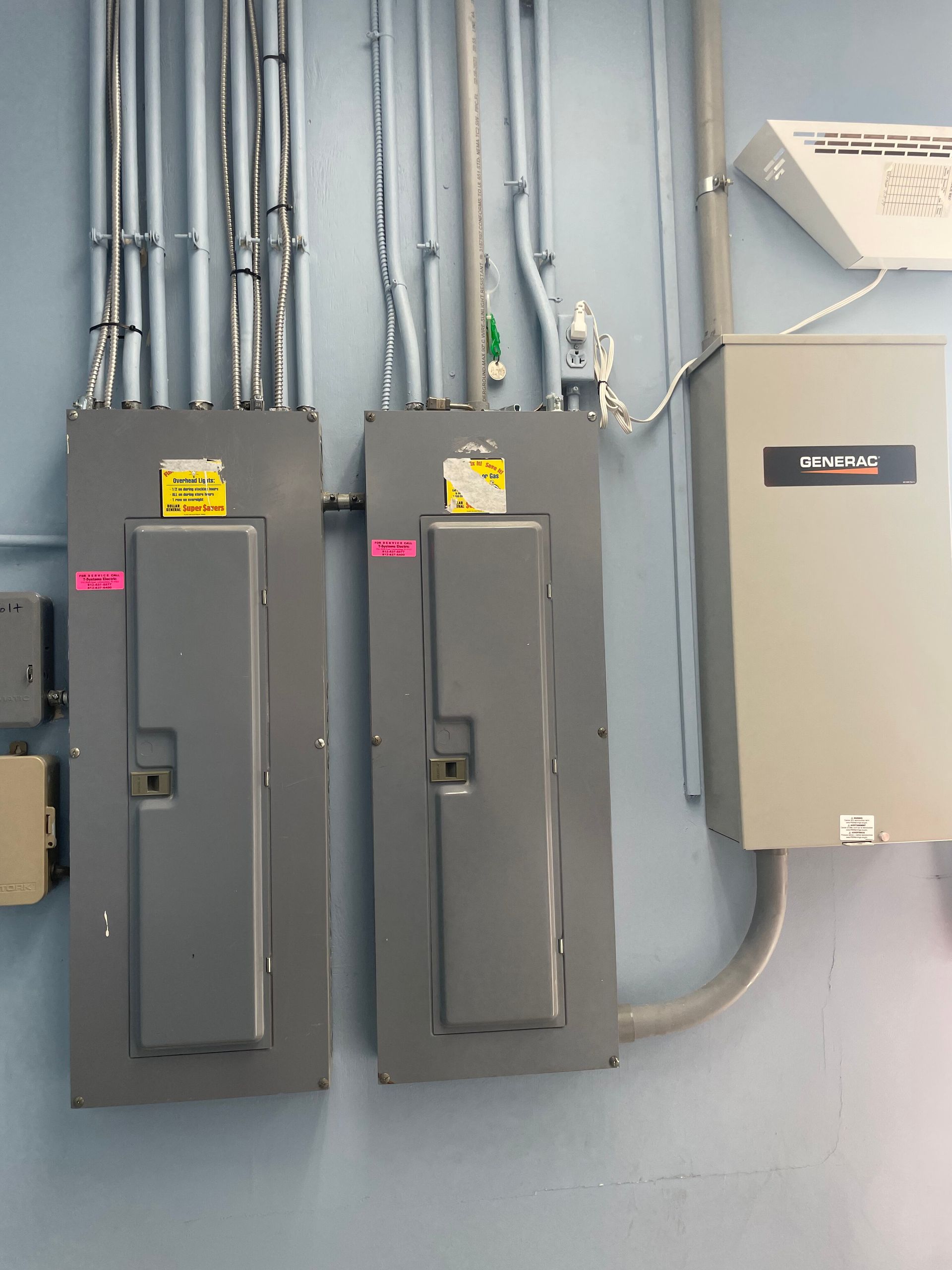 Two gray electrical panels and a beige box on a blue wall. Pipes and wires run above.