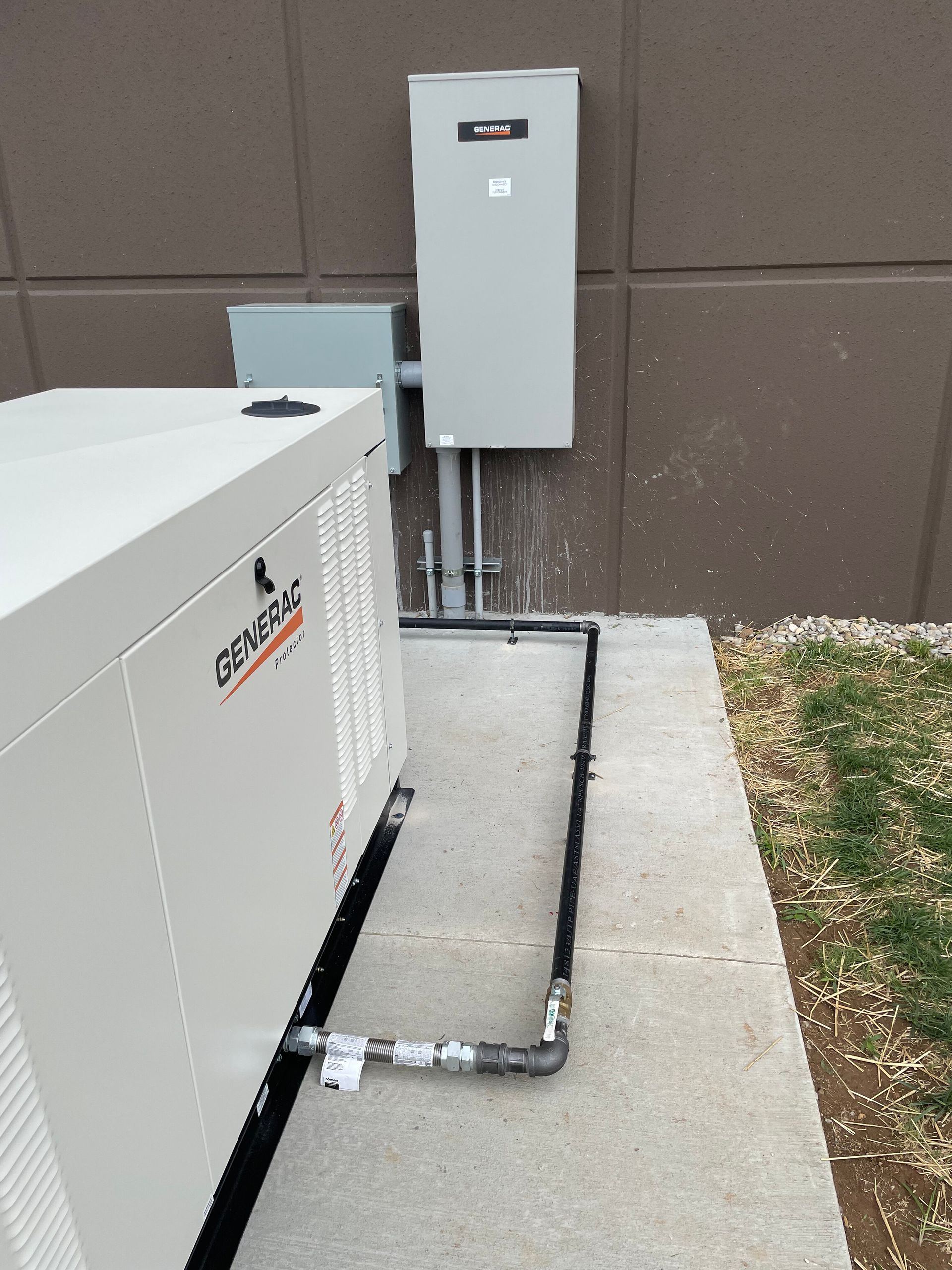 Generator beside a building with electrical boxes and black piping on a concrete pad.