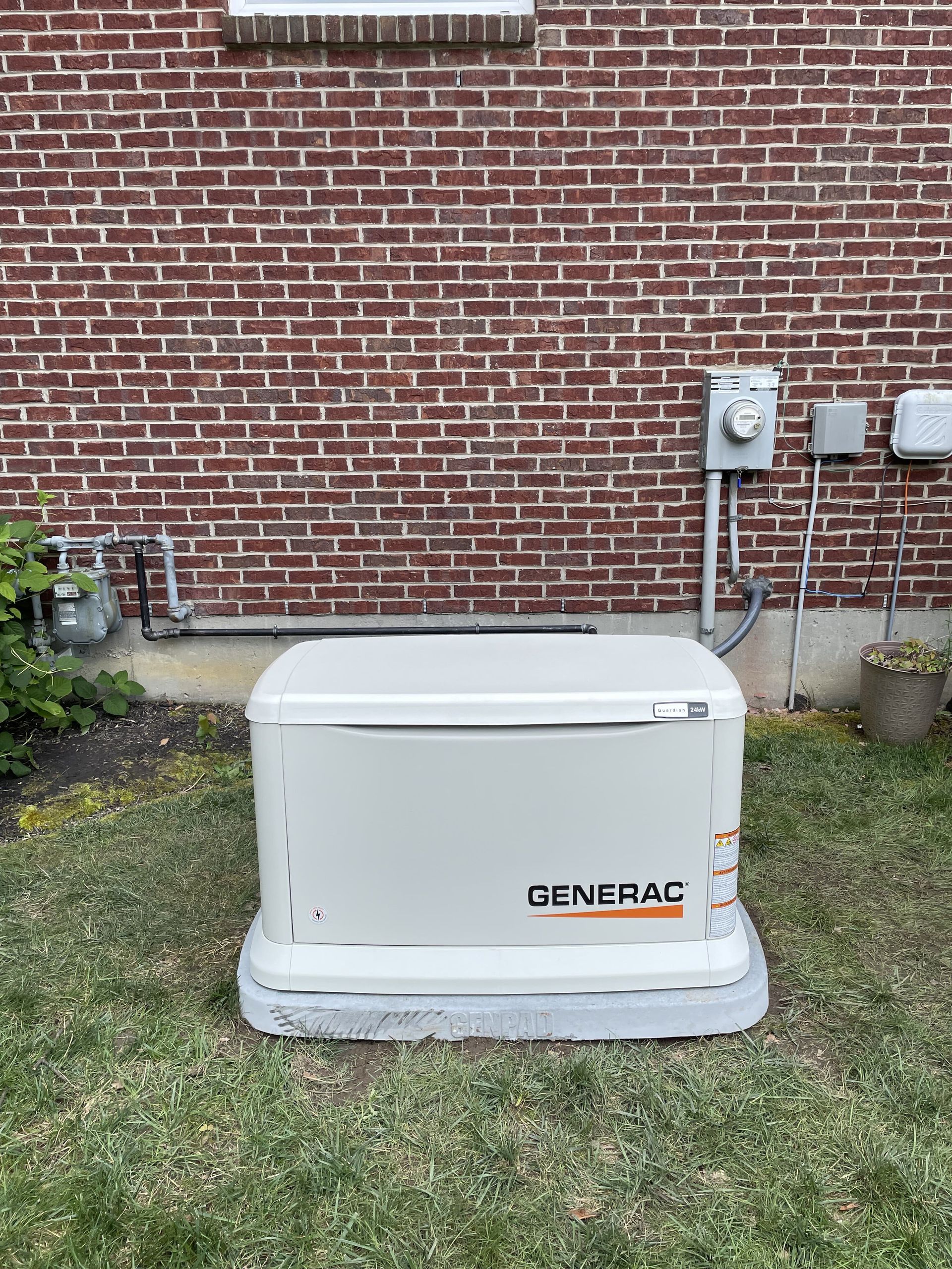 Generac generator in a yard near a brick building with electrical boxes.