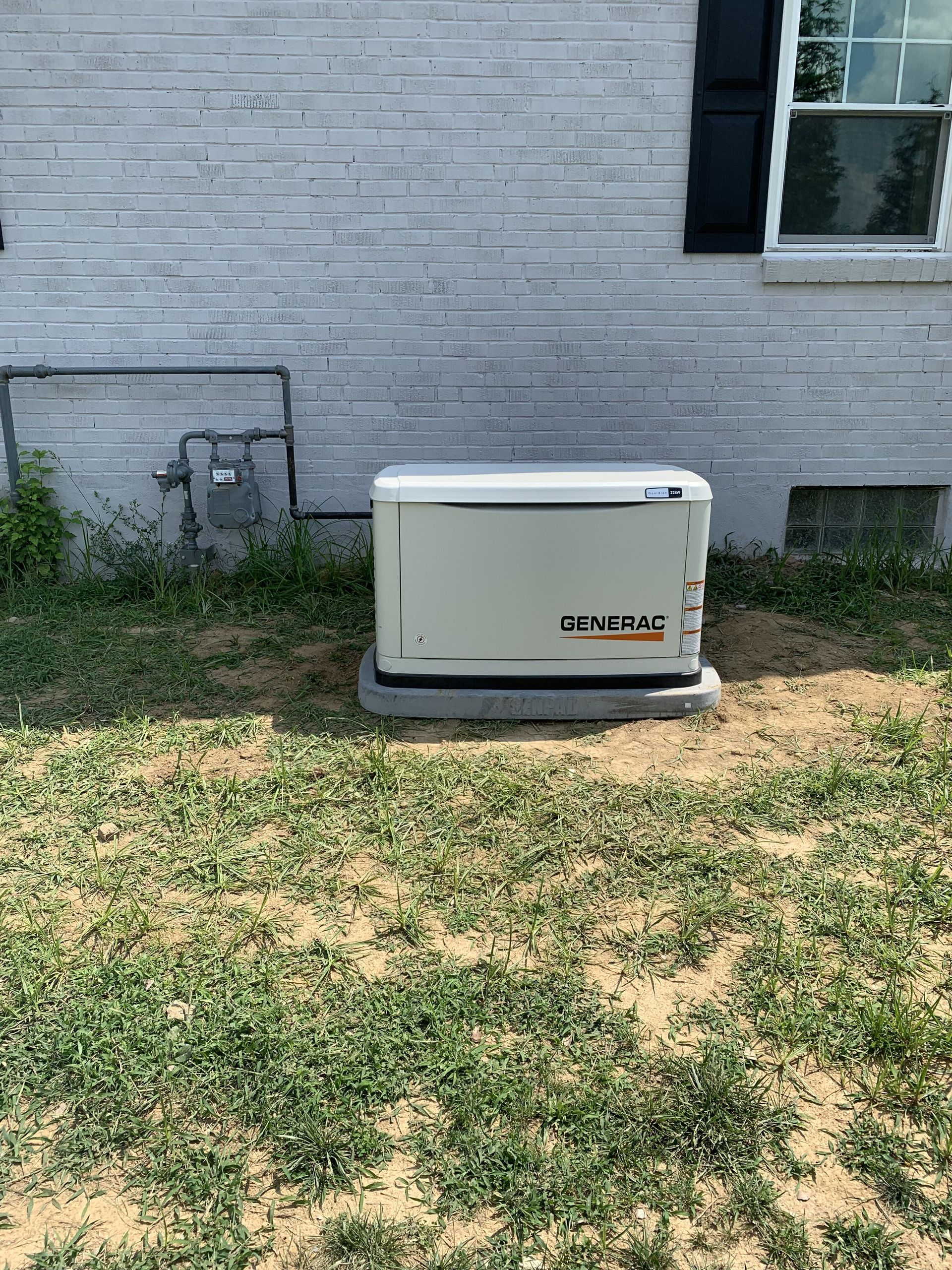 Generator outside a brick building on a concrete pad, in a yard with weeds.