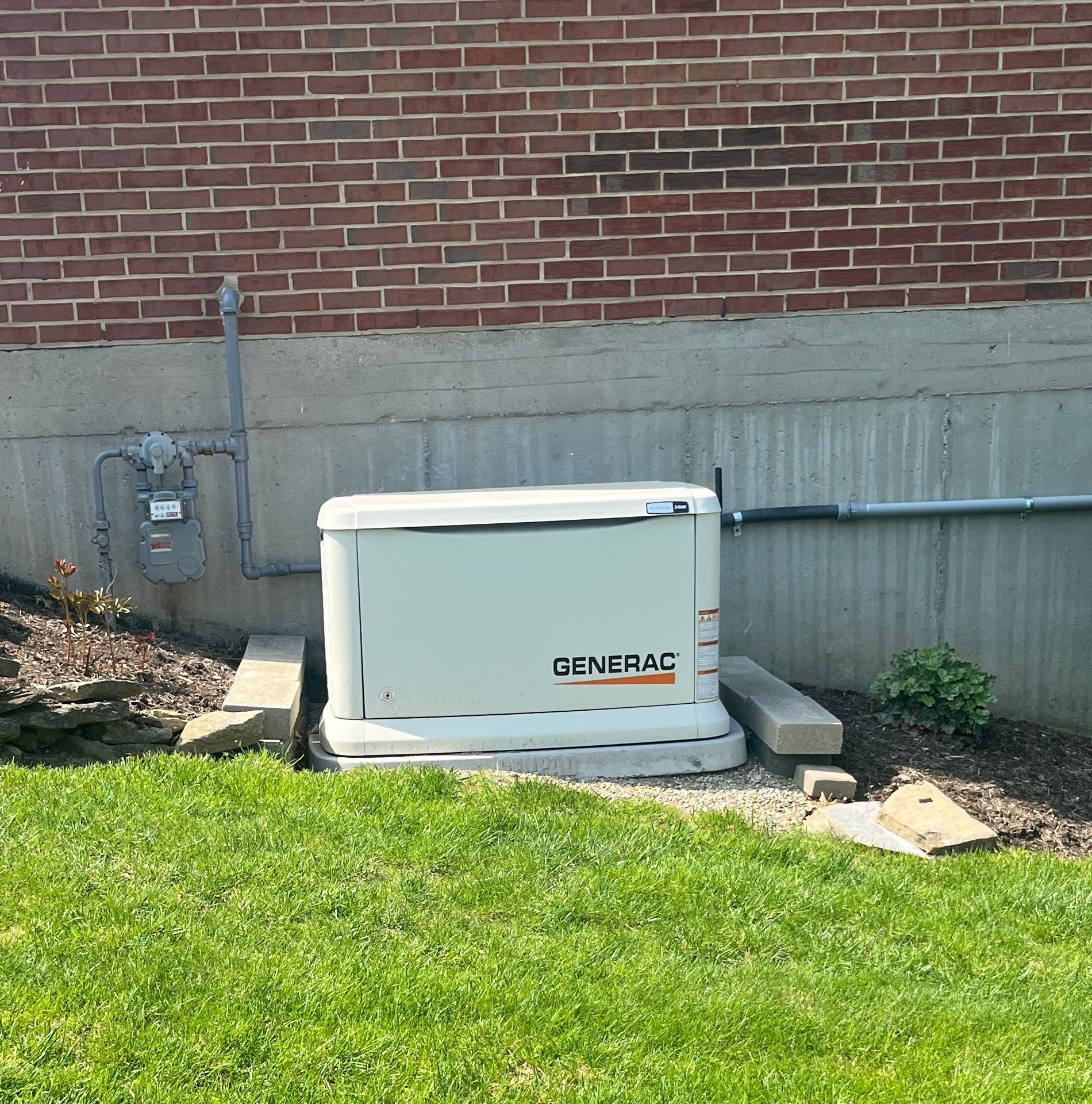 A white Generac generator outside a brick building. Connected to gas and electrical lines.