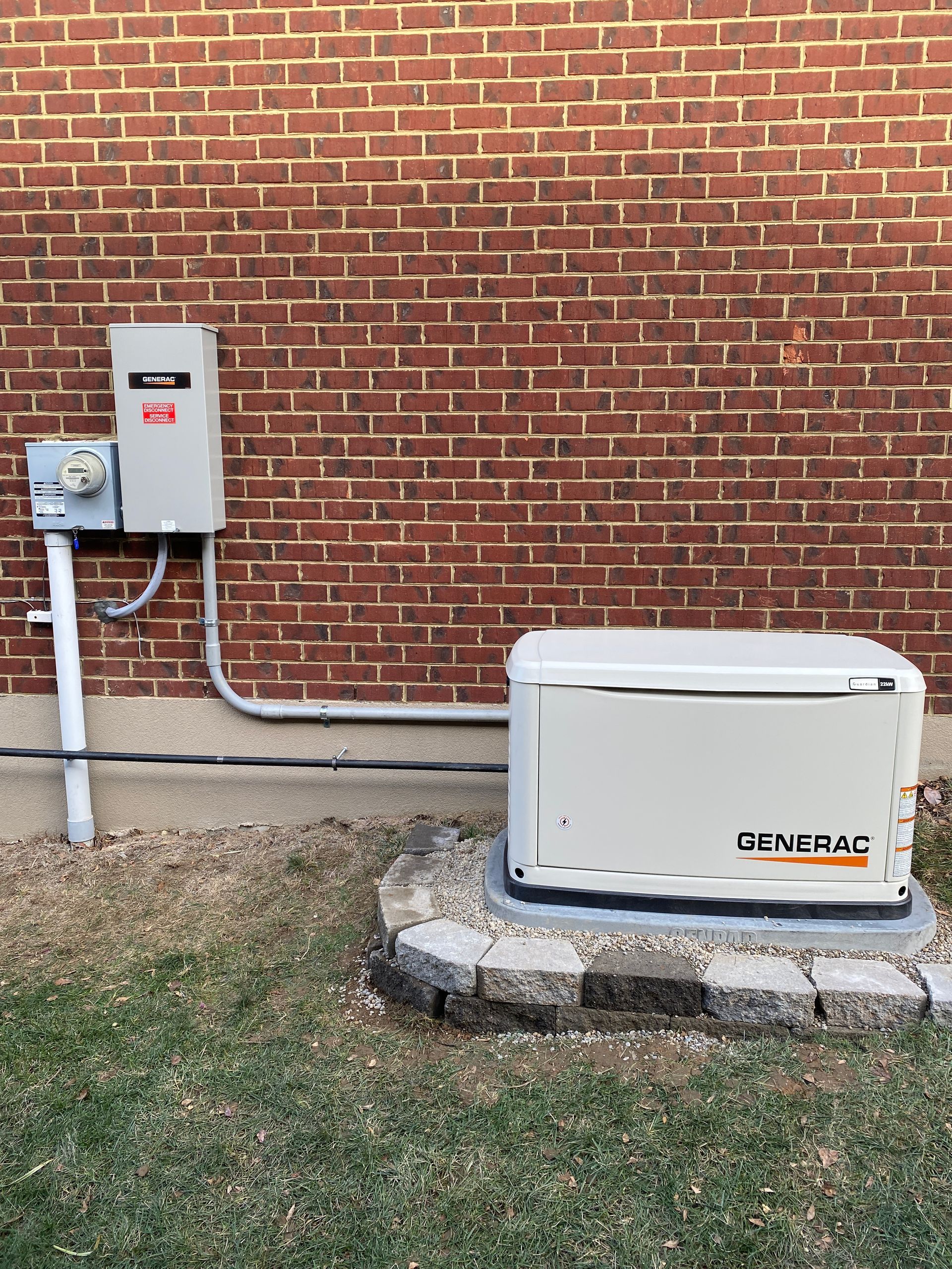 A Generac home generator on a concrete pad next to a brick wall. Gray box and conduit.