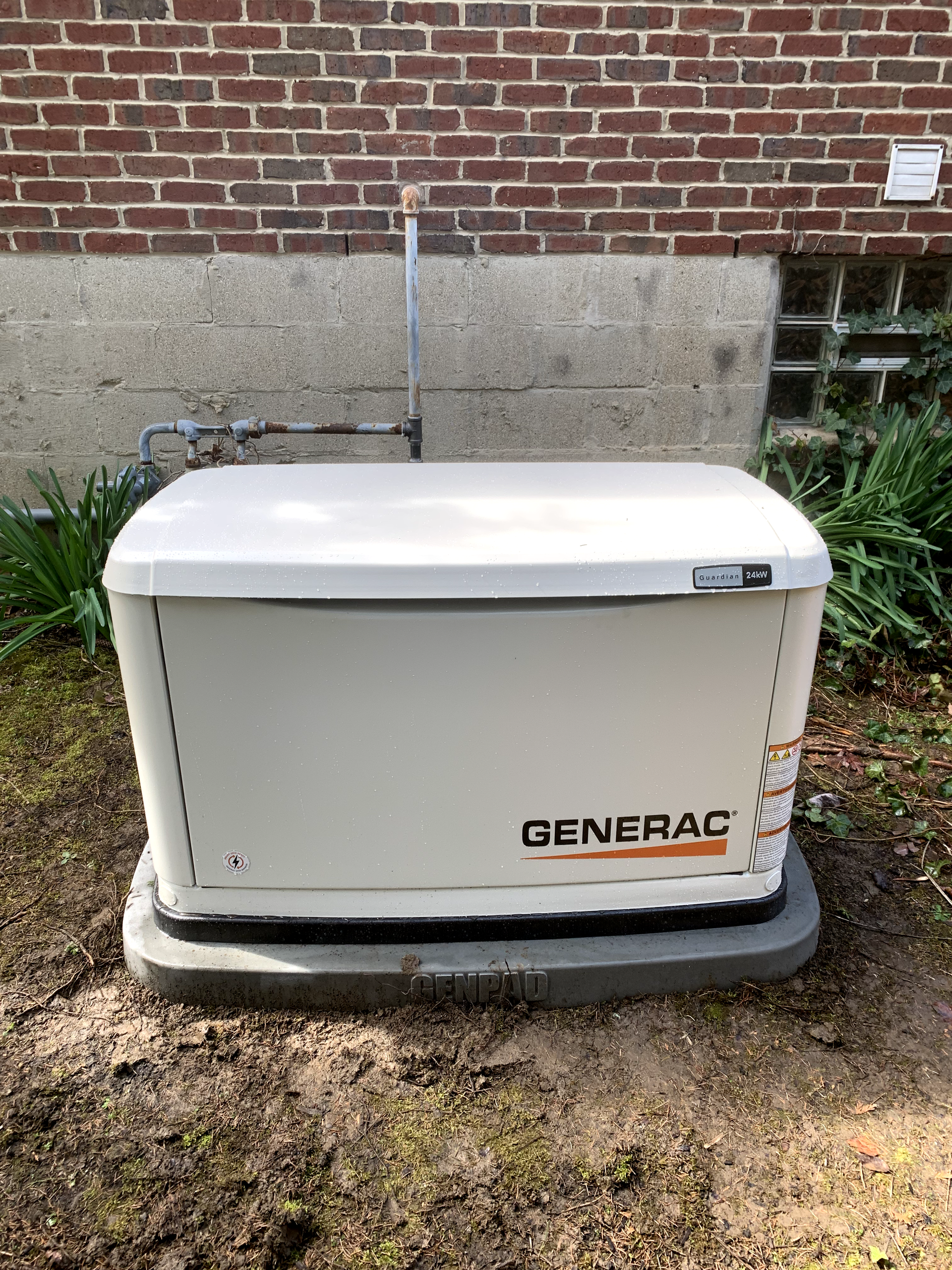 White Generac generator on a concrete pad next to a brick building.