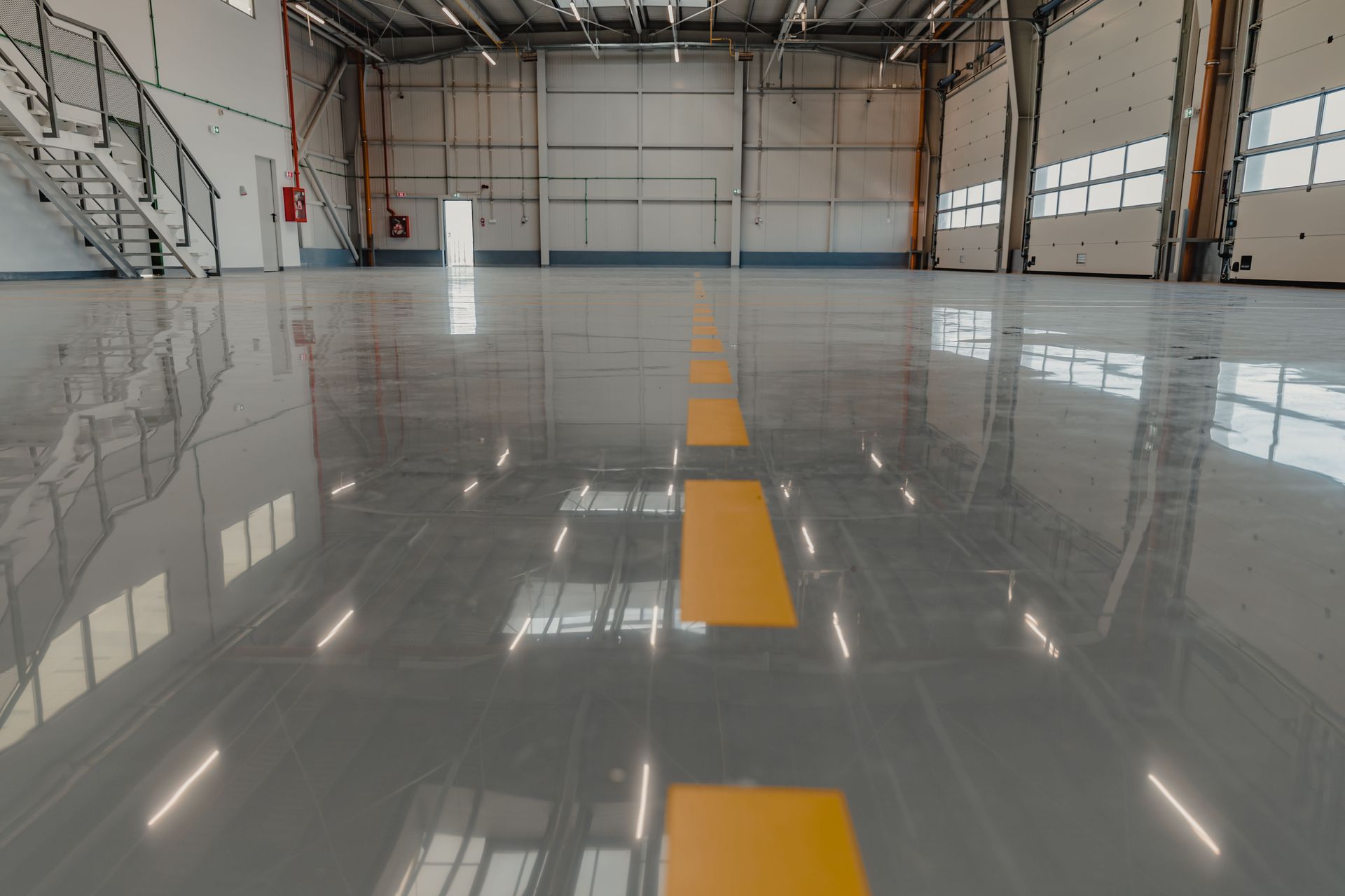 Empty hangar with shiny gray floor, yellow line, and open doors.