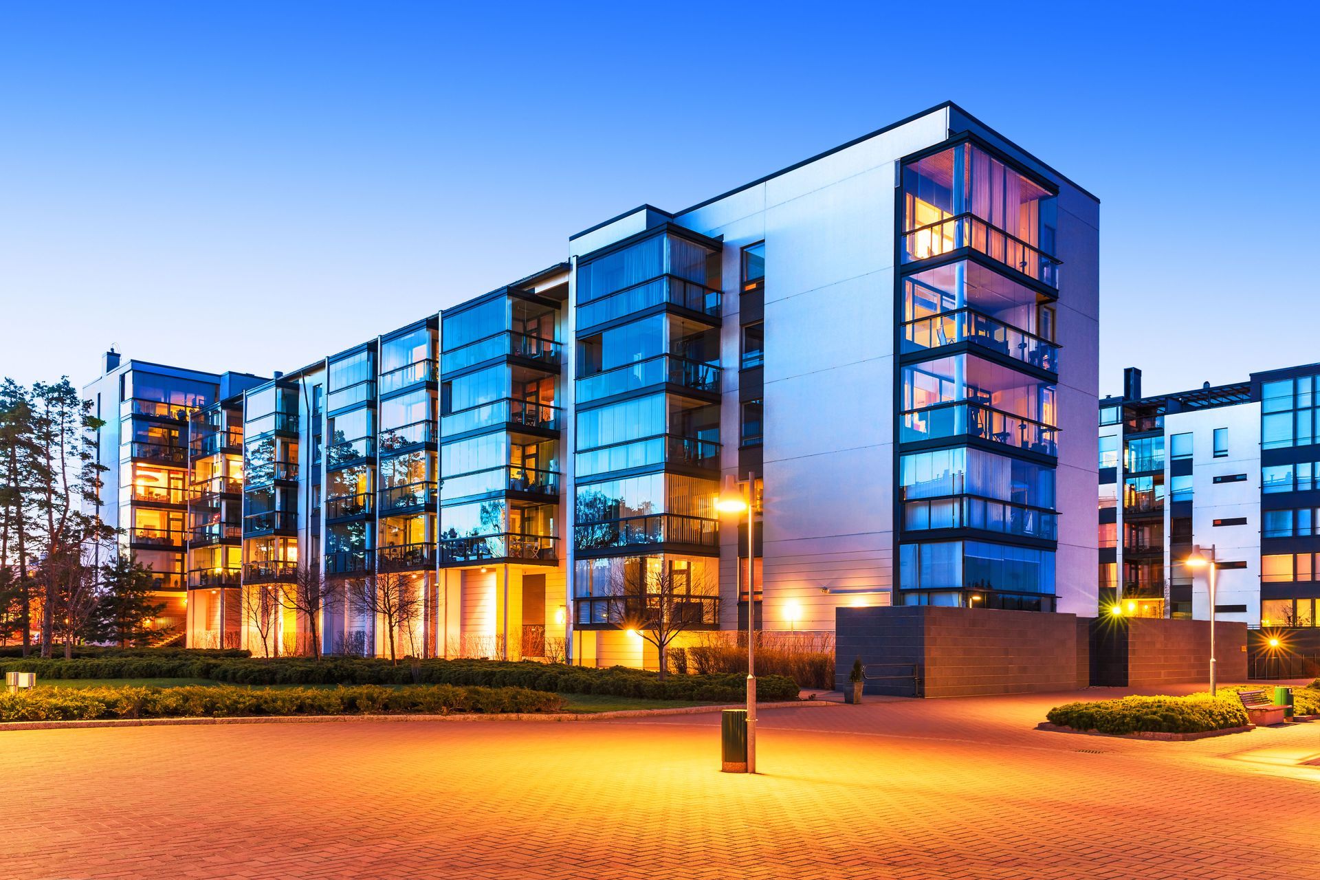 Modern apartment building with glass balconies illuminated at dusk.
