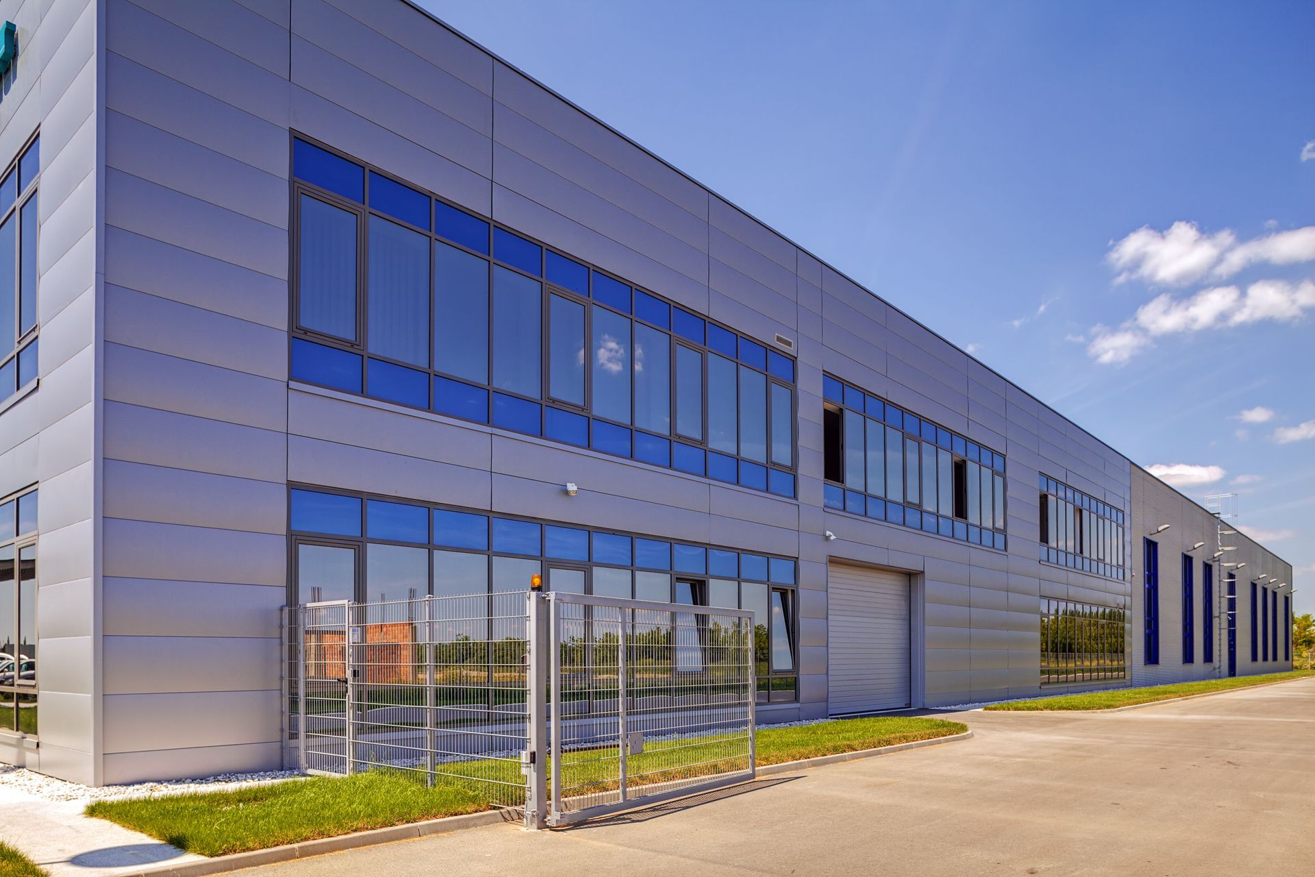 Modern industrial building with blue-tinted windows and metallic facade under a sunny sky.