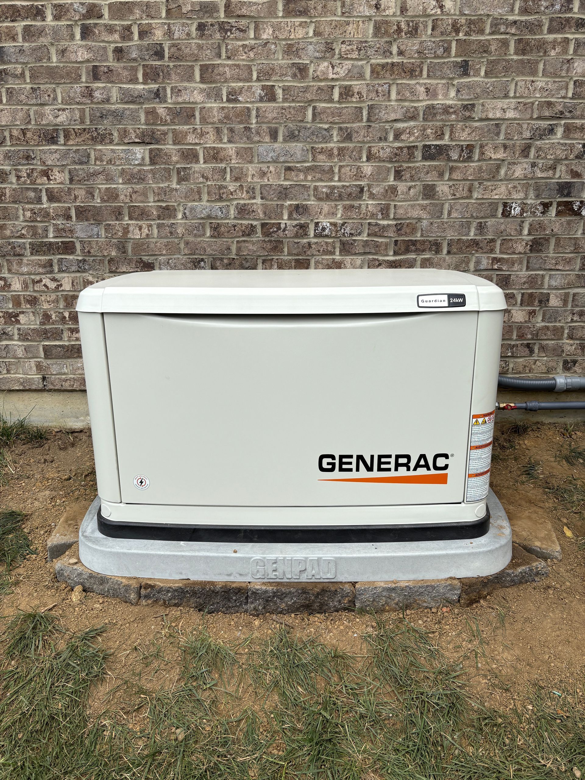 Generac home generator on a concrete pad next to a brick wall.
