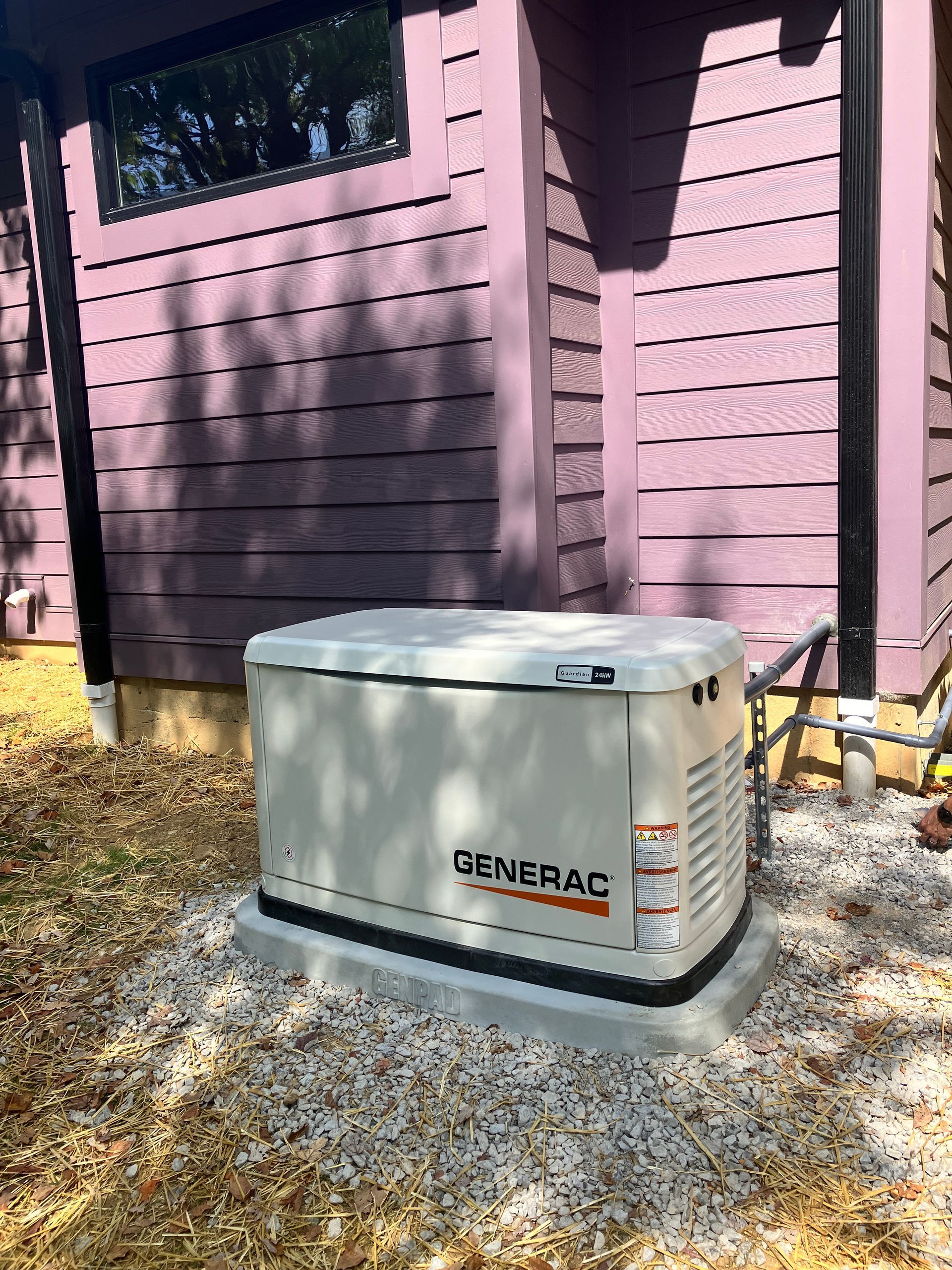 Generac generator outside a lavender-sided house.  The generator sits on a concrete pad covered in gravel.