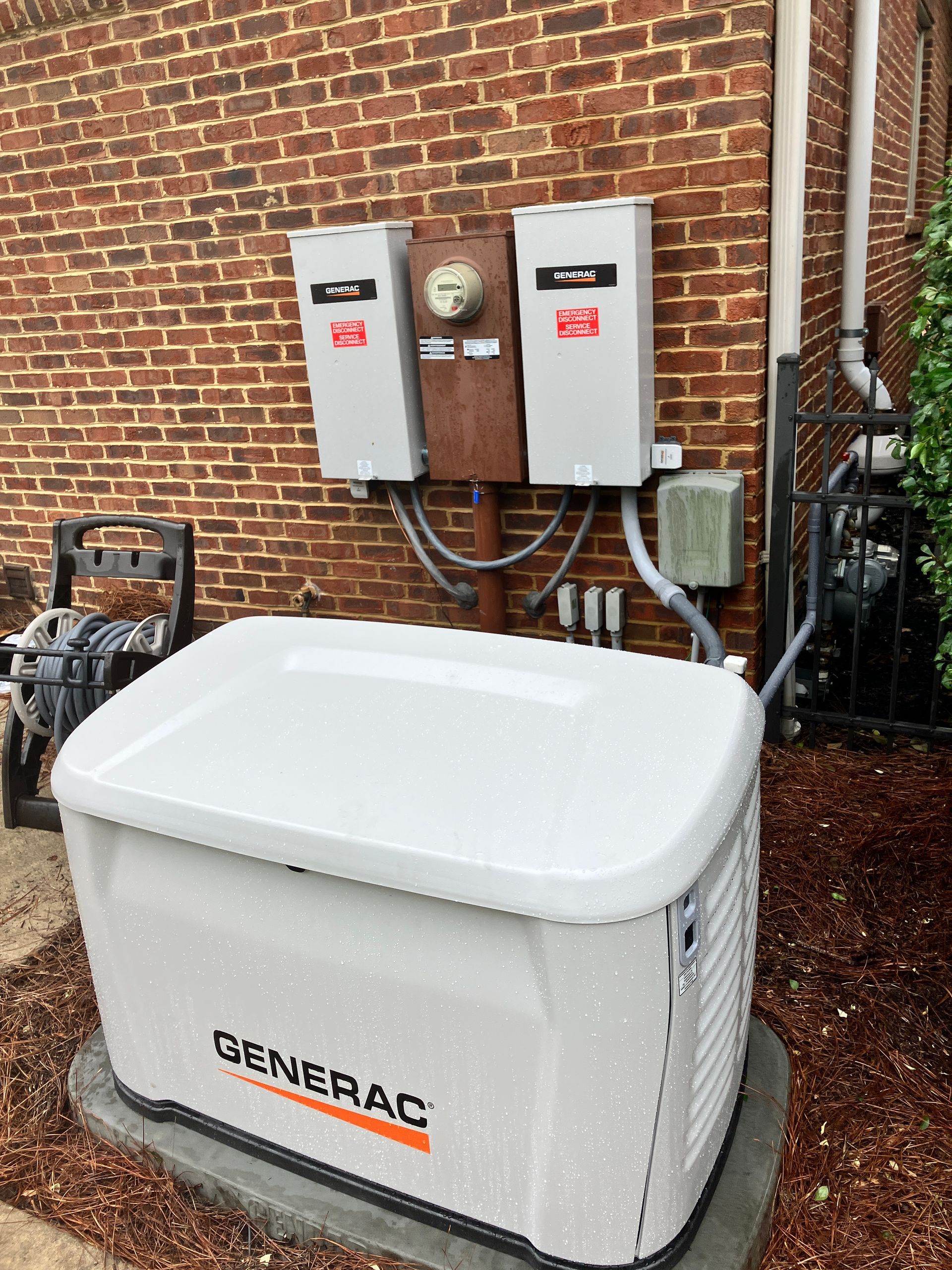 A white Generac generator next to a brick wall with electrical components.