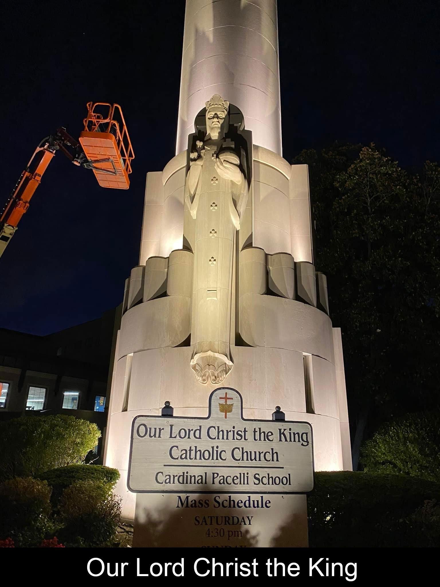 Illuminated church tower with a statue of Jesus. Sign reads