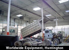 Dump truck raised in a Worldwide Equipment Huntington garage for repairs. White building, gray trucks.