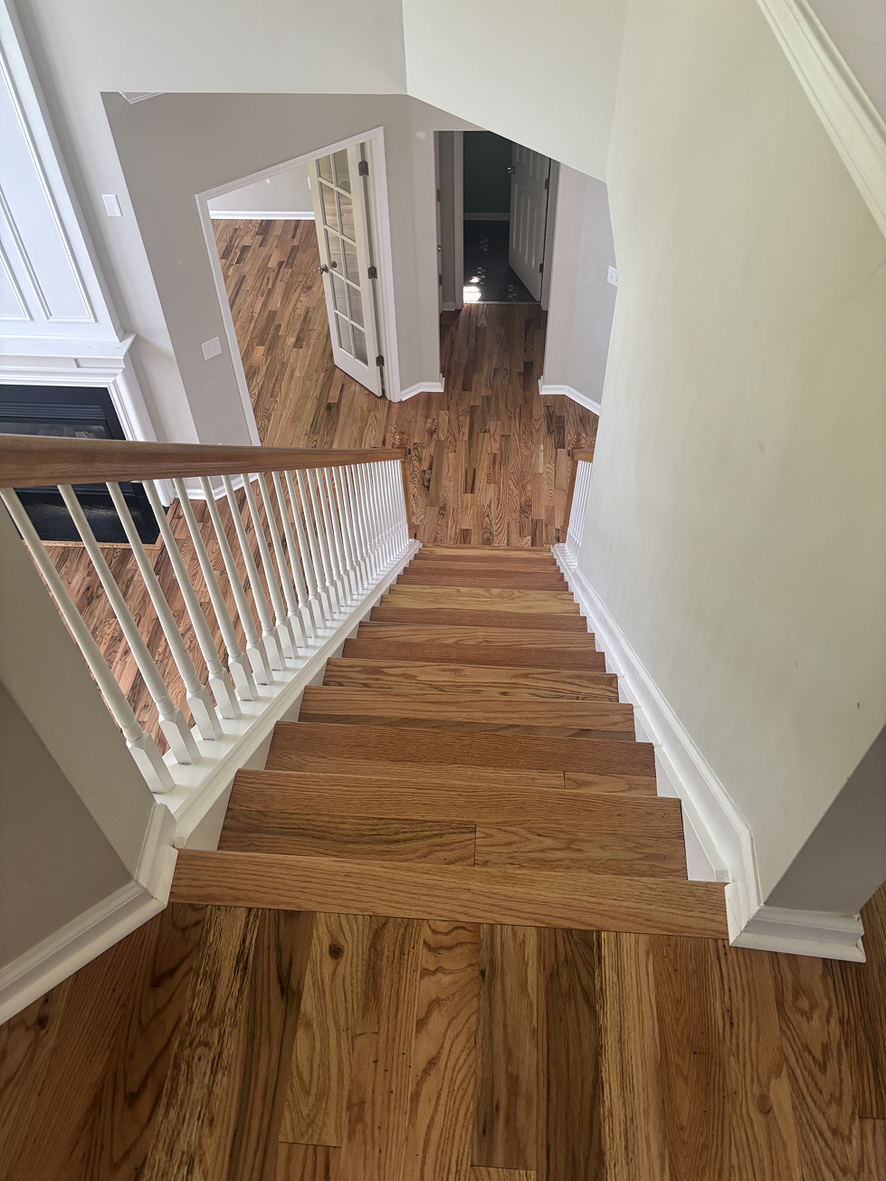 Wooden staircase leading down from a hallway with light wood floors and white railings.