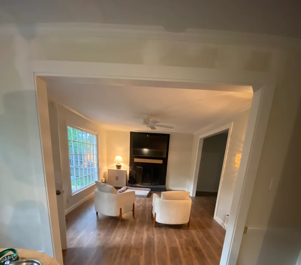 Wooden floor in a room with a window, light brown walls, and white trim.