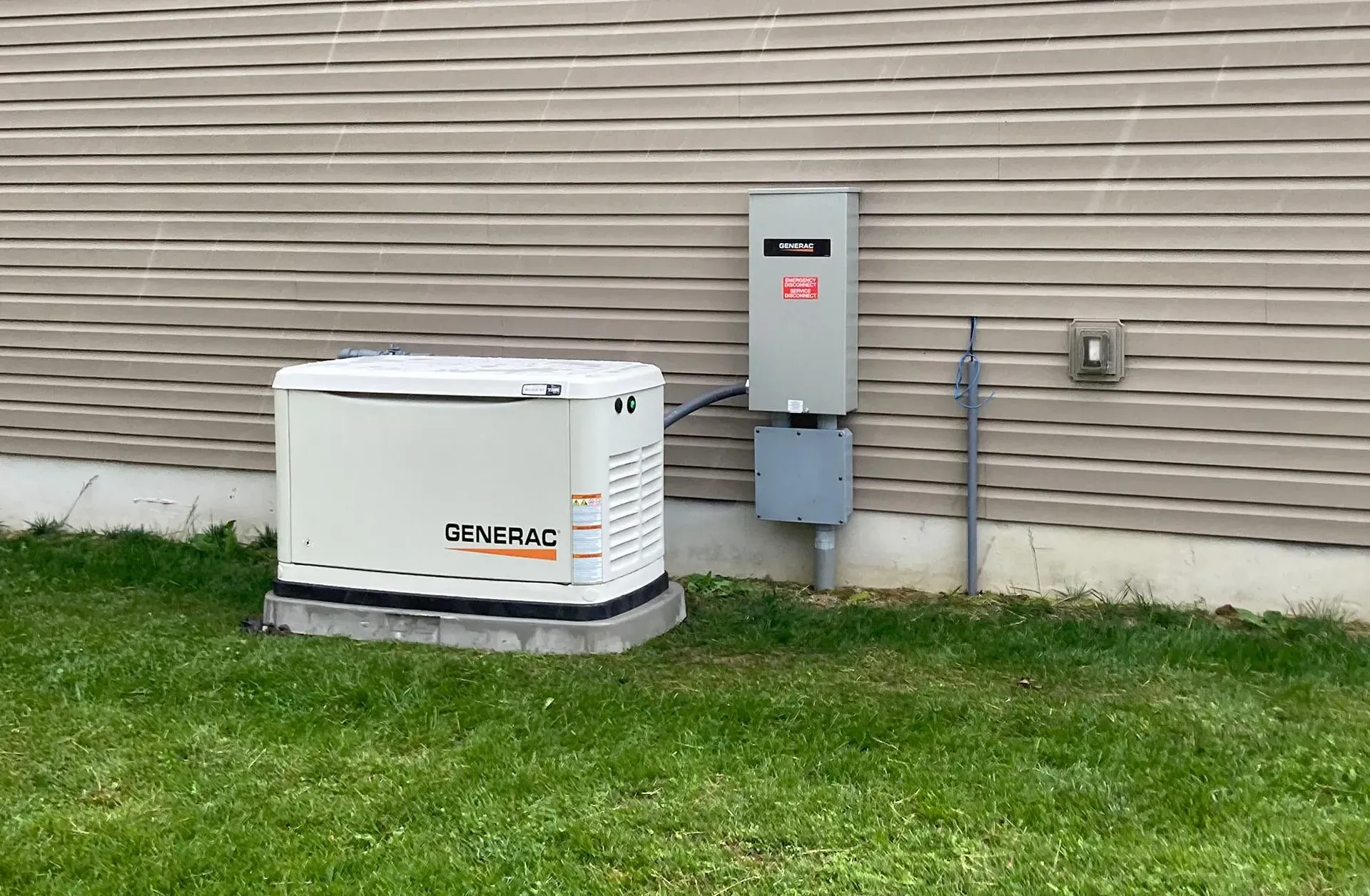 White generator beside a house wall on a grassy lawn, with electrical meter and conduit nearby